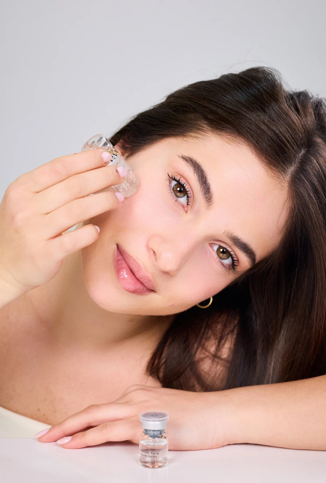 Woman applying the VYA micro infusion device to her cheek, Peptide Anti-Aging Ampoule Serum on the table